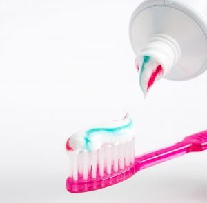 a pink toothbrush with red blue striped toothpaste