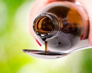pouring a pharmaceutical active liquid on a spoon. natural green background